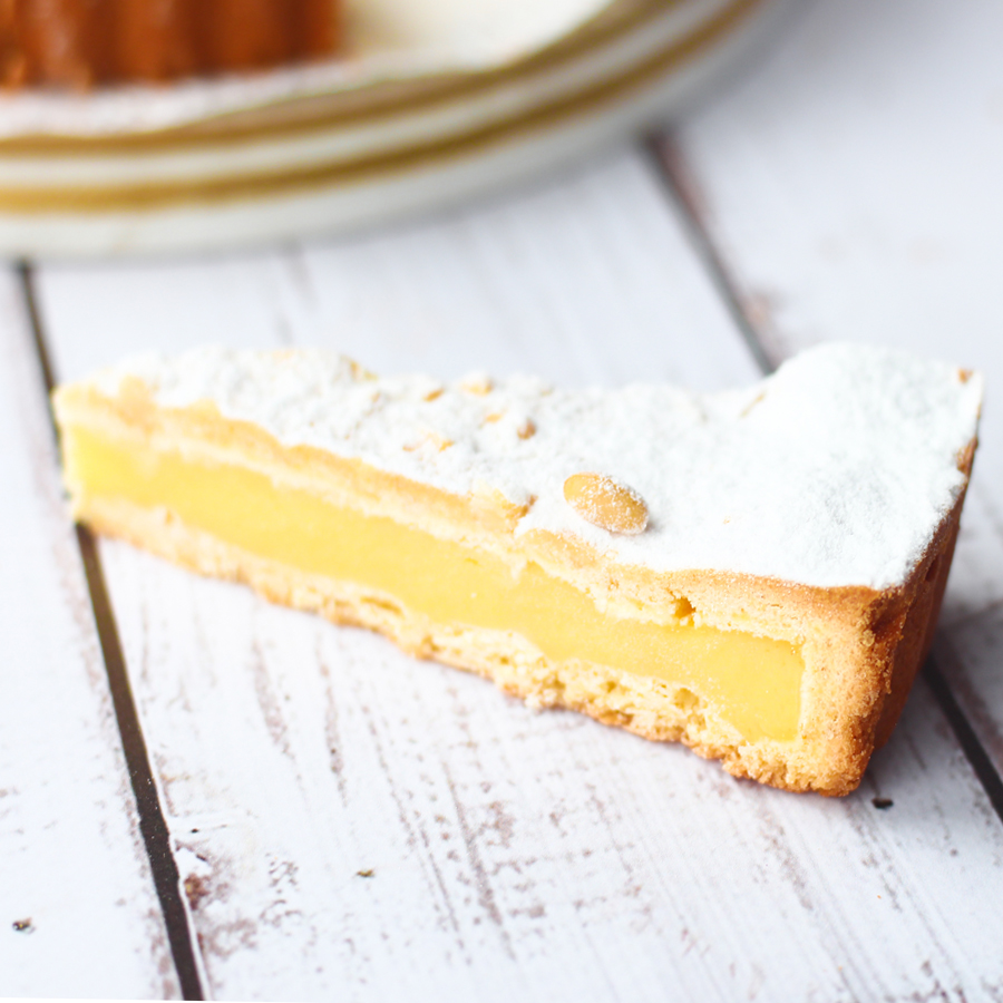 Основа торта из песочного теста, начинка из заварного ванильного крема с легкими цитрусовыми нотками. Сверху торт украшен колотыми орешками итальянской сосны - пинии и присыпан пудрой. изображение 1