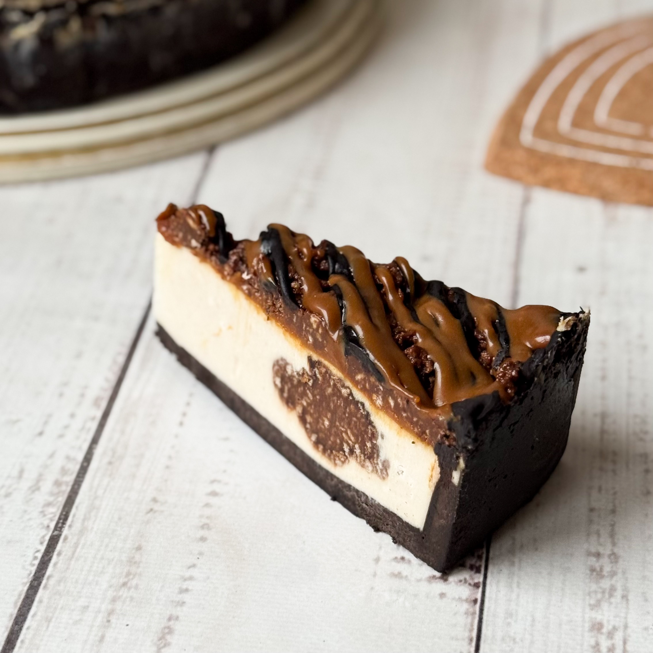 Классический сливочно-сырный чизкейк Нью-Йорк на подложке из песочного шоколадного теста с начинкой из шоколадного ганаша и карамельного кранча. Сверху чизкейк украшен карамельным кранчем, арахисом, карамелью и шоколадным муссом. изображение 3