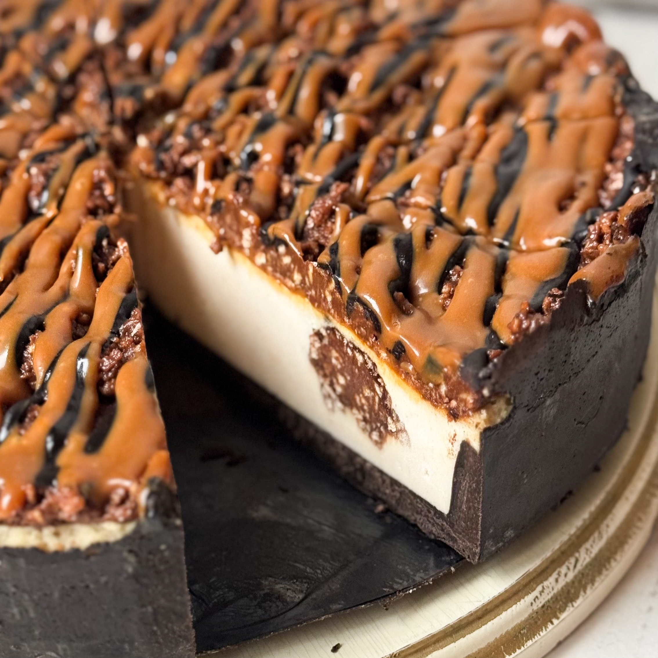 Классический сливочно-сырный чизкейк Нью-Йорк на подложке из песочного шоколадного теста с начинкой из шоколадного ганаша и карамельного кранча. Сверху чизкейк украшен карамельным кранчем, арахисом, карамелью и шоколадным муссом. изображение 2