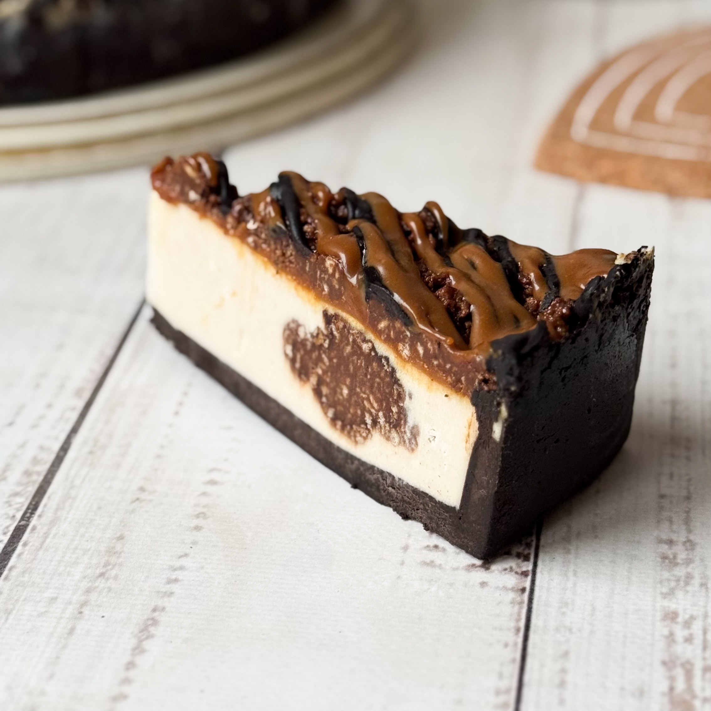 Классический сливочно-сырный чизкейк Нью-Йорк на подложке из песочного шоколадного теста с начинкой из шоколадного ганаша и карамельного кранча. Сверху чизкейк украшен карамельным кранчем, арахисом, карамелью и шоколадным муссом. изображение 3