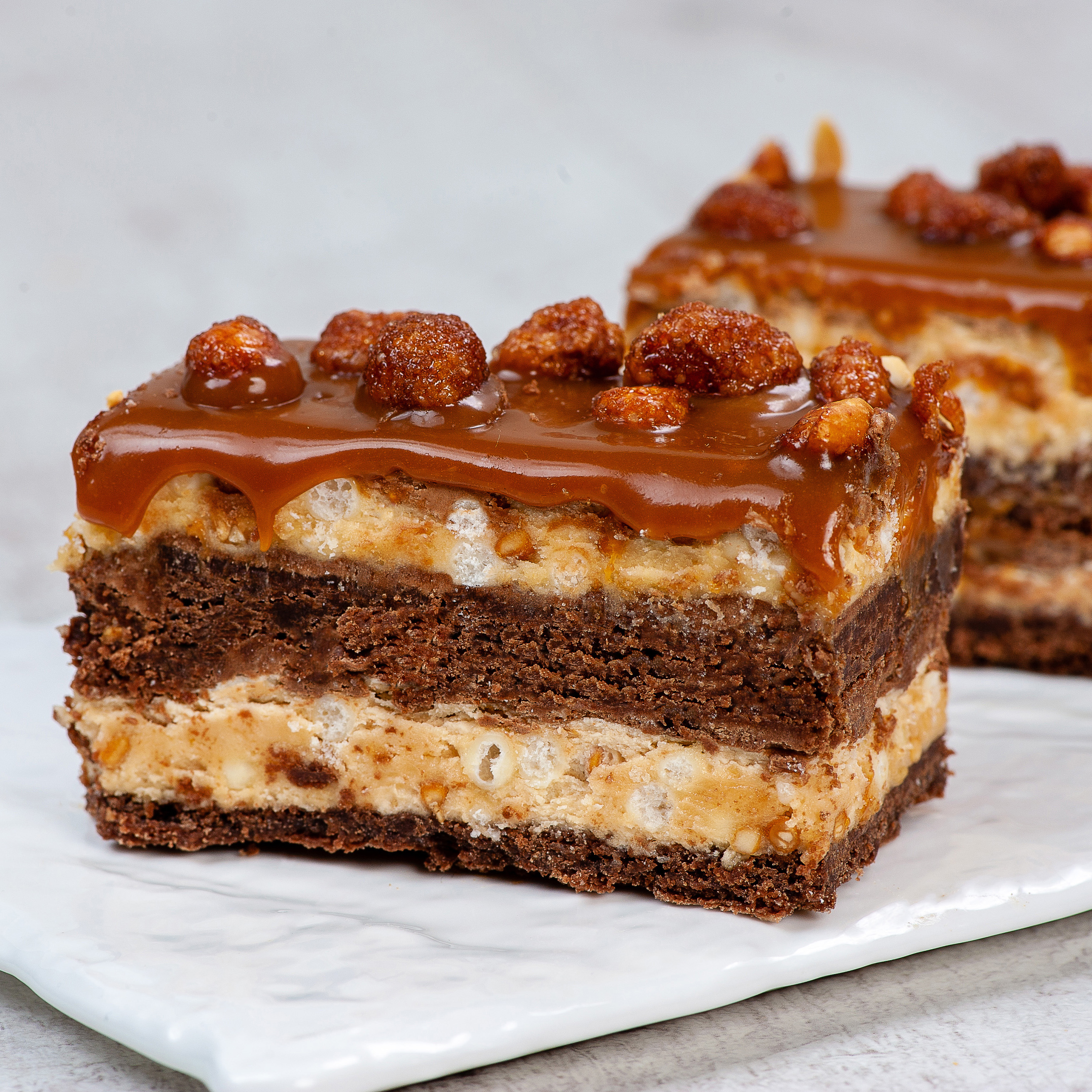 Классический брауни со слоями сливочной карамели, пралине и молочного шоколада. Сверху пирожное украшено карамелизированным арахисом и залит плотным слоем мягкой карамели изображение 1