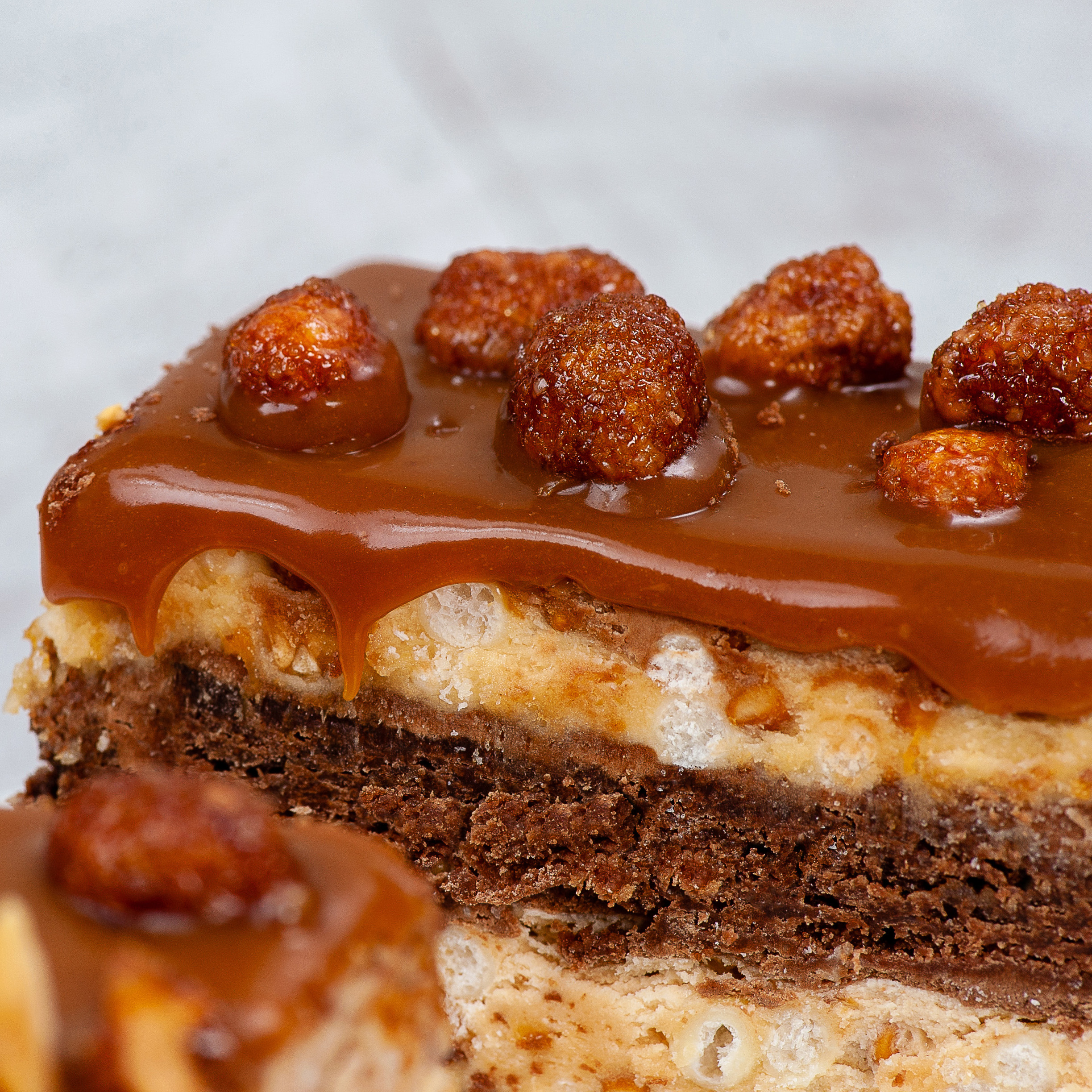 Классический брауни со слоями сливочной карамели, пралине и молочного шоколада. Сверху пирожное украшено карамелизированным арахисом и залит плотным слоем мягкой карамели изображение 2