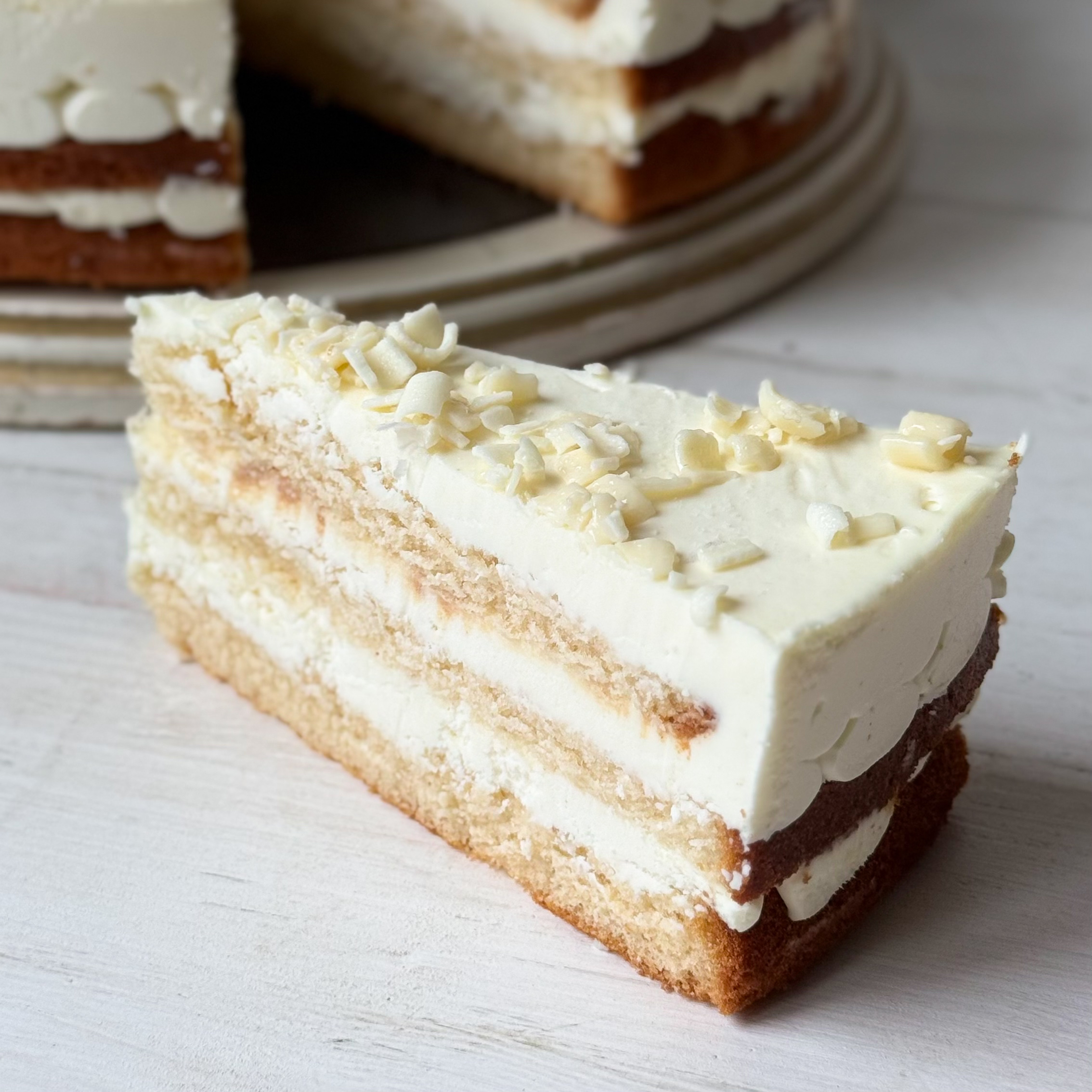 Изысканный торт из слоев нежного бисквита и творожного крема. Сверху торт украшен посыпкой из белого шоколада. изображение 3