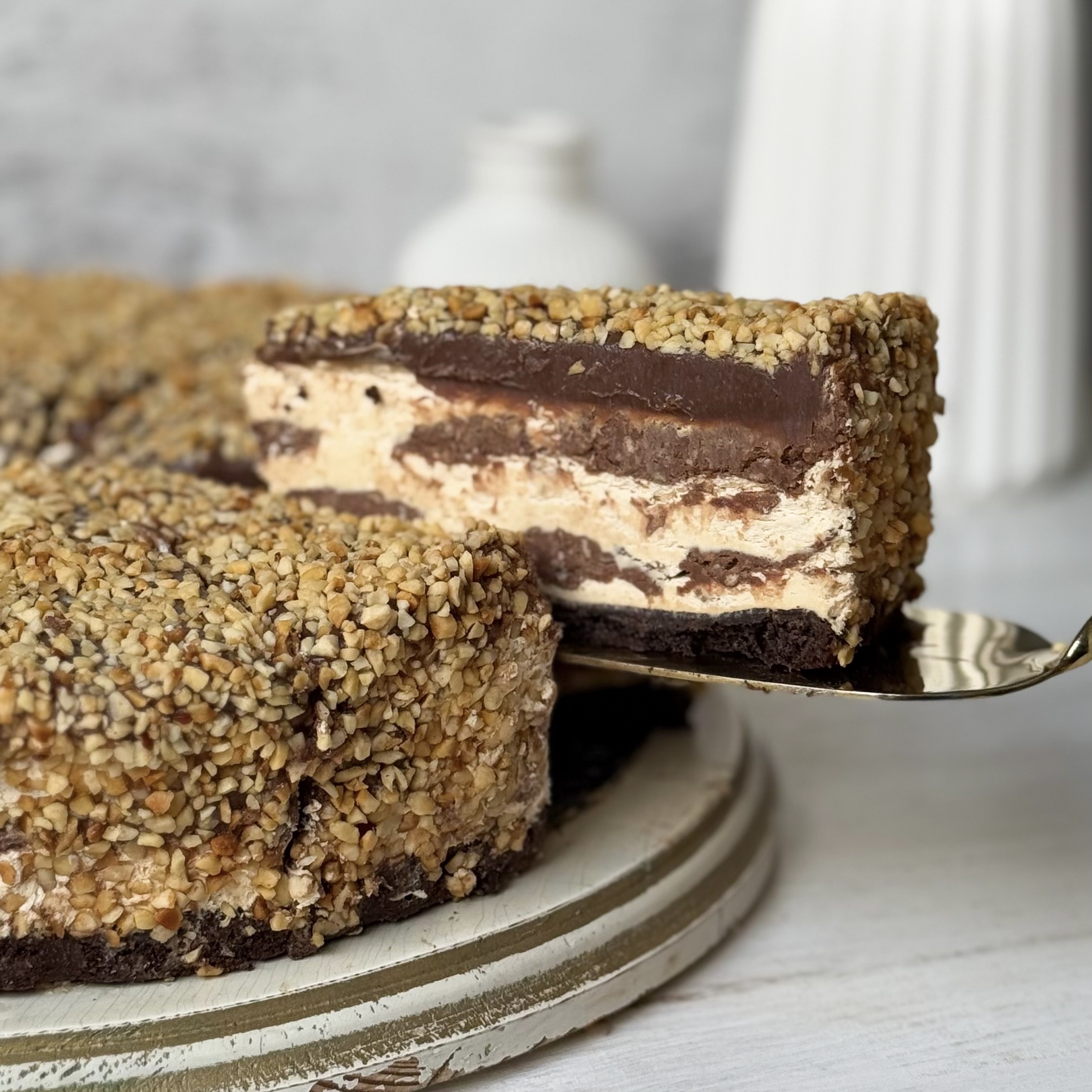 Нежный торт с сердцевиной из фундучного пралине, молочного шоколада, крема из взбитых сливок и хрустящей крошки на тонкой шоколадной подложке. Торт залит толстым шоколадным слоем и украшен дроблёным орехом. изображение 1