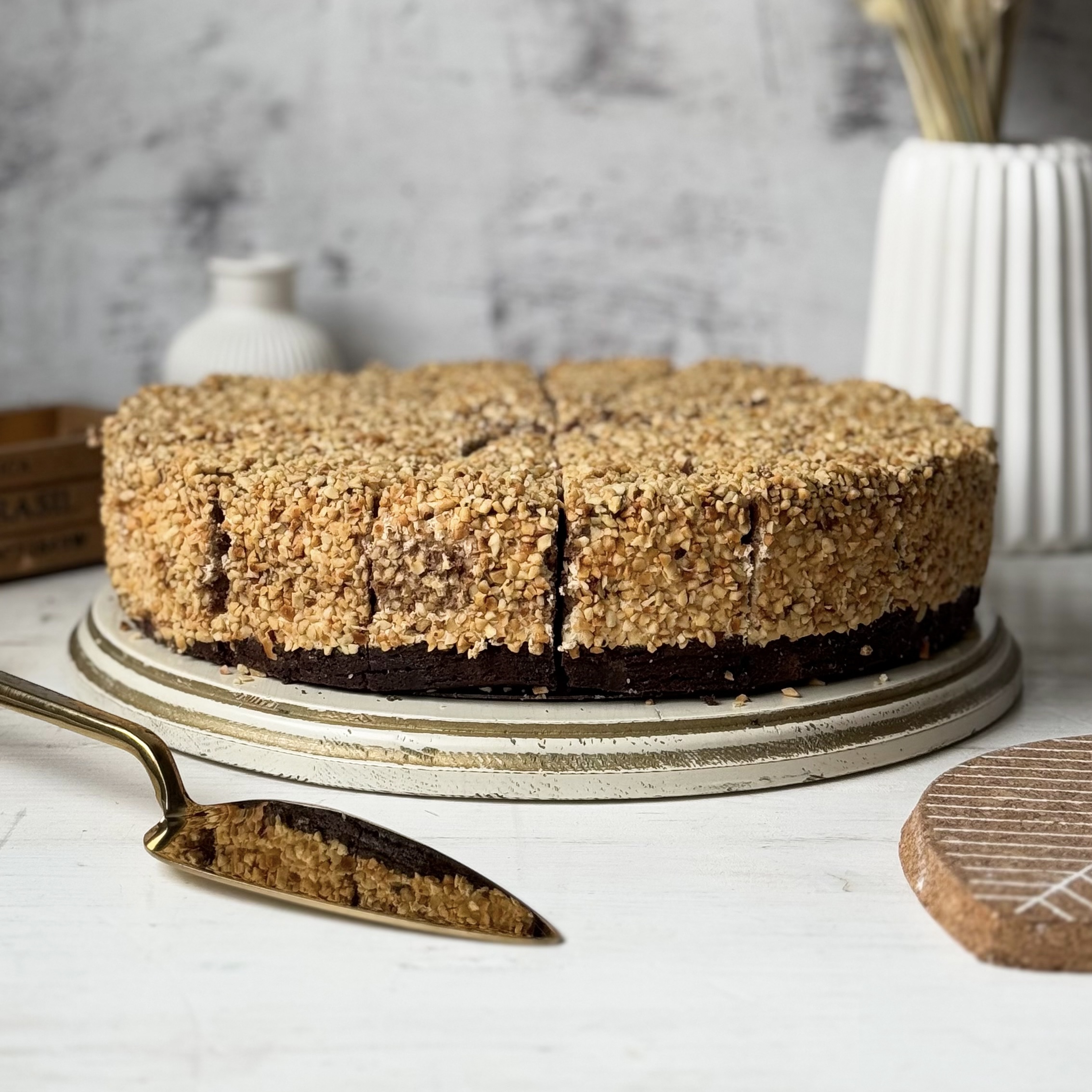 Нежный торт с сердцевиной из фундучного пралине, молочного шоколада, крема из взбитых сливок и хрустящей крошки на тонкой шоколадной подложке. Торт залит толстым шоколадным слоем и украшен дроблёным орехом. изображение 2