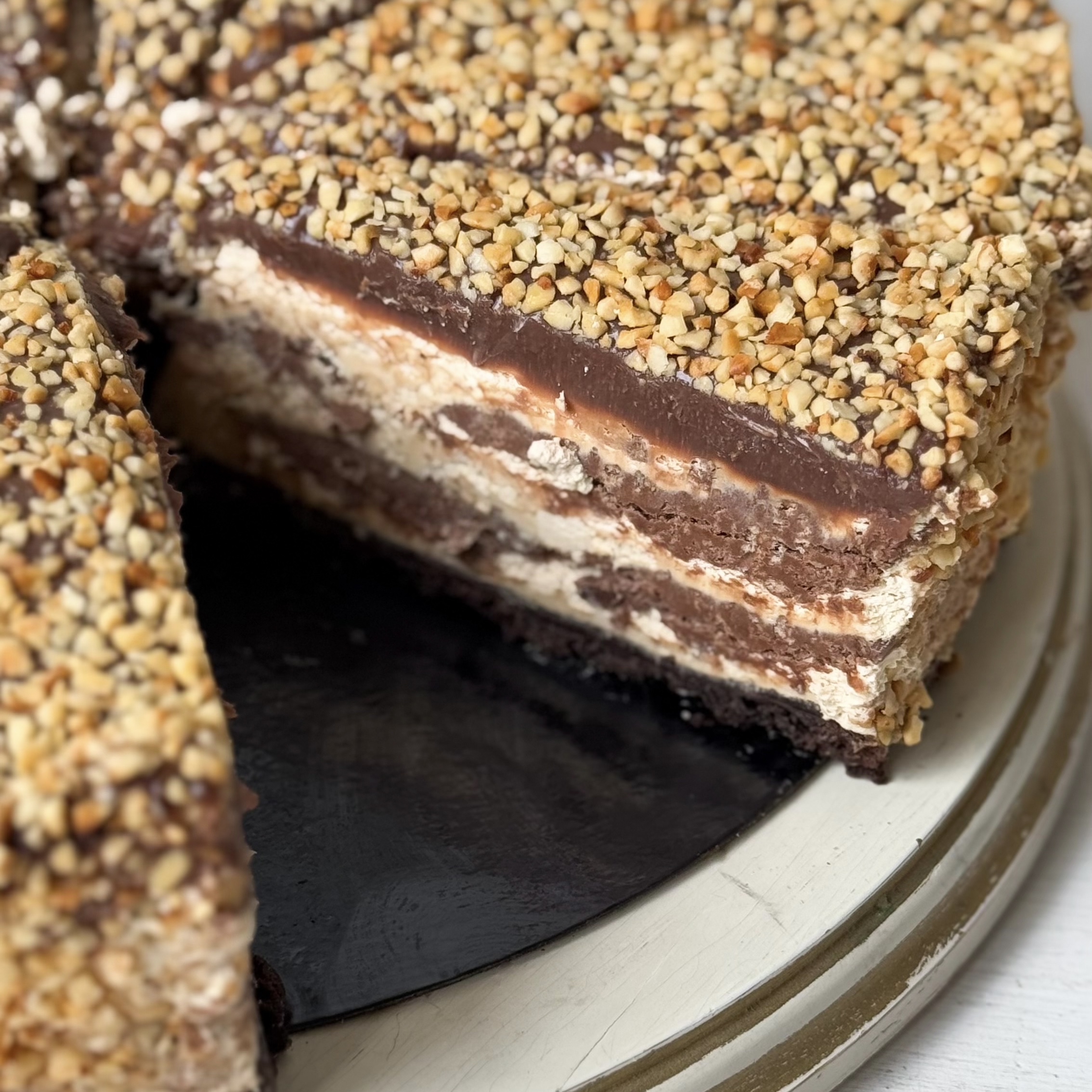 Нежный торт с сердцевиной из фундучного пралине, молочного шоколада, крема из взбитых сливок и хрустящей крошки на тонкой шоколадной подложке. Торт залит толстым шоколадным слоем и украшен дроблёным орехом. изображение 4