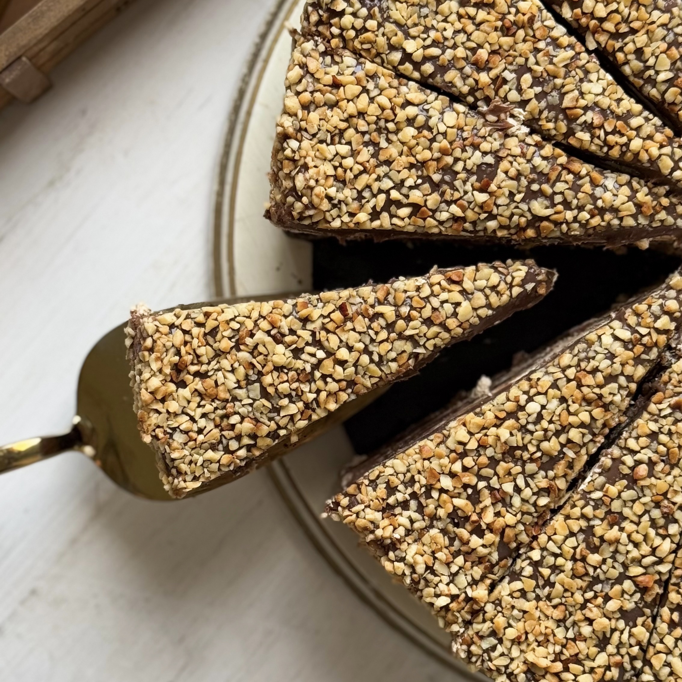 Нежный торт с сердцевиной из фундучного пралине, молочного шоколада, крема из взбитых сливок и хрустящей крошки на тонкой шоколадной подложке. Торт залит толстым шоколадным слоем и украшен дроблёным орехом. изображение 5