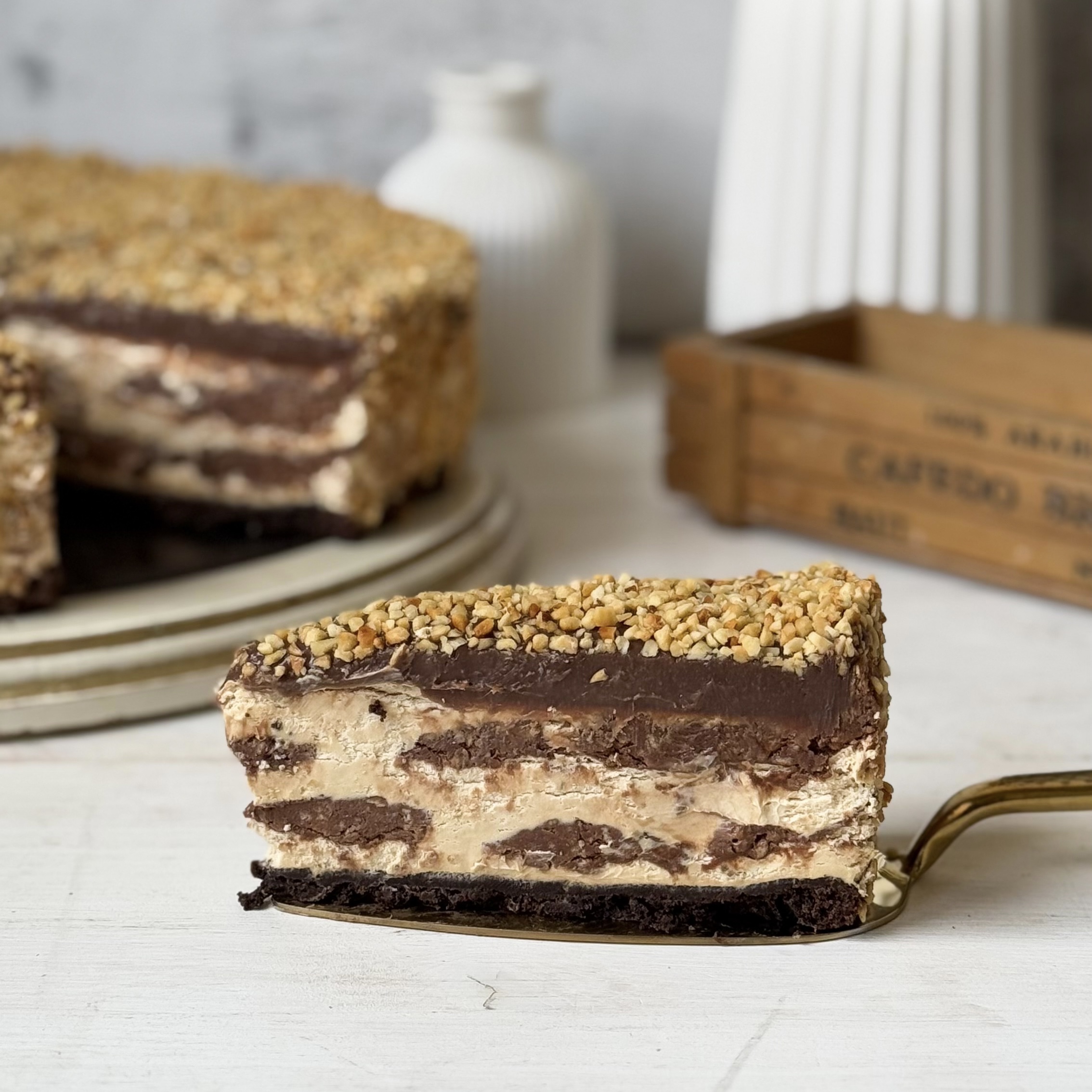 Нежный торт с сердцевиной из фундучного пралине, молочного шоколада, крема из взбитых сливок и хрустящей крошки на тонкой шоколадной подложке. Торт залит толстым шоколадным слоем и украшен дроблёным орехом. изображение 6