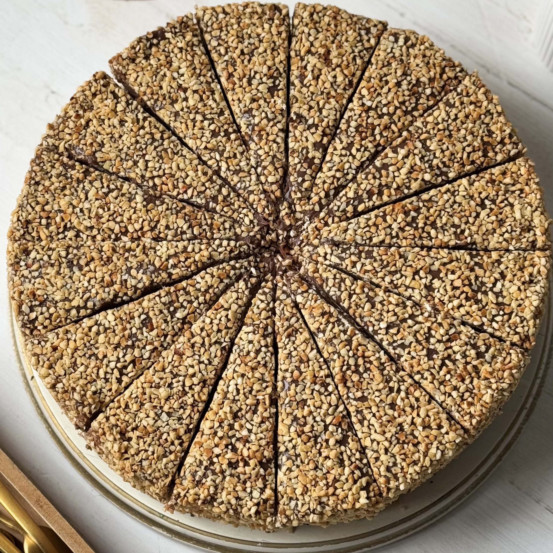 Нежный торт с сердцевиной из фундучного пралине, молочного шоколада, крема из взбитых сливок и хрустящей крошки на тонкой шоколадной подложке. Торт залит толстым шоколадным слоем и украшен дроблёным орехом. изображение 7