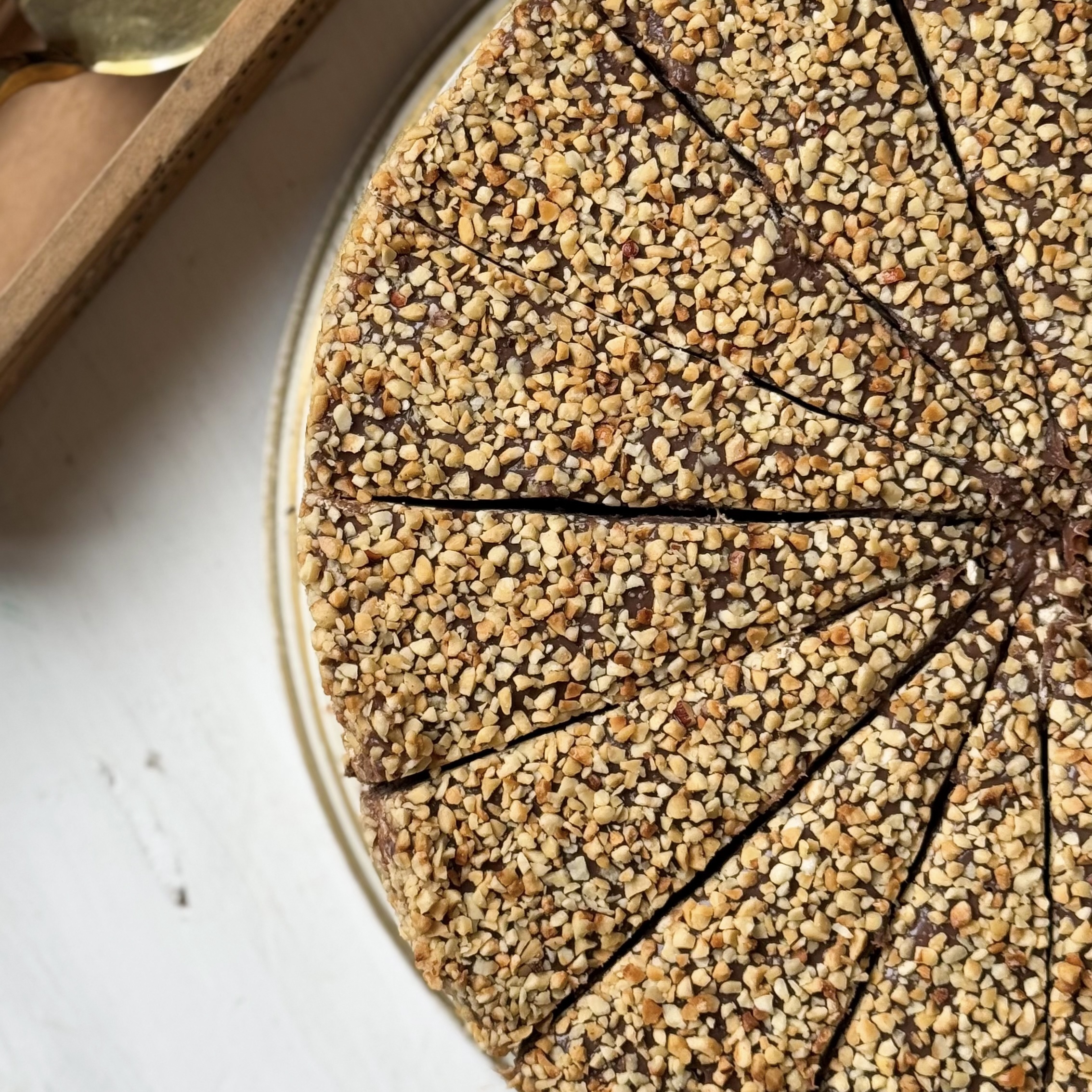 Нежный торт с сердцевиной из фундучного пралине, молочного шоколада, крема из взбитых сливок и хрустящей крошки на тонкой шоколадной подложке. Торт залит толстым шоколадным слоем и украшен дроблёным орехом. изображение 9